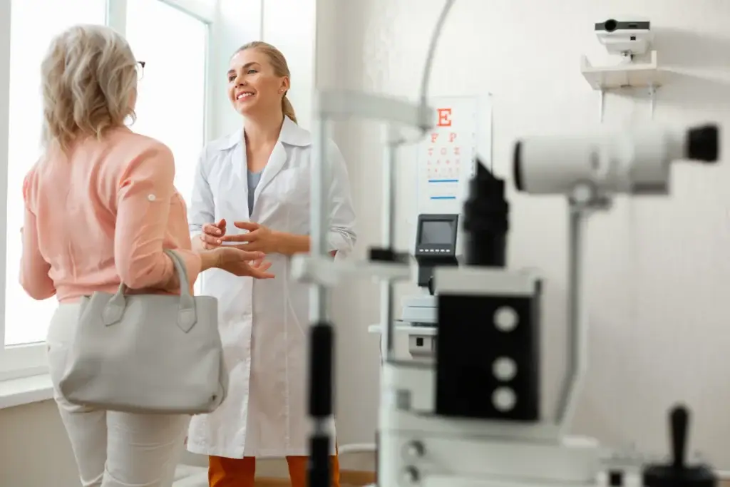 a woman in a white coat talking to a woman in a room with medical equipment